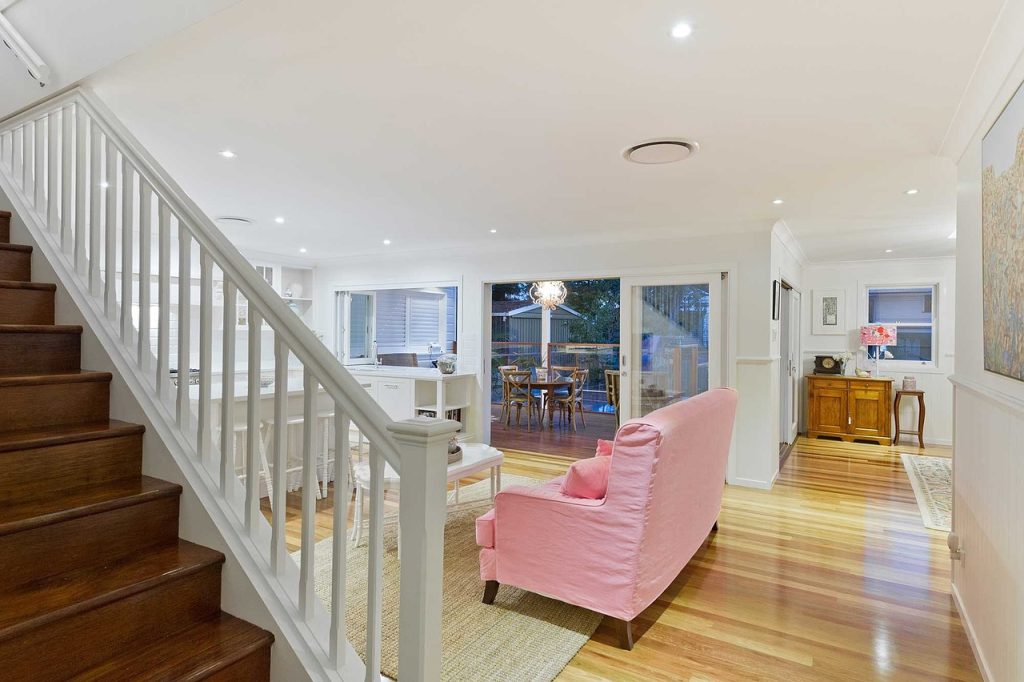 A white staircase ascends to a living room featuring a stylish pink couch, creating a welcoming atmosphere