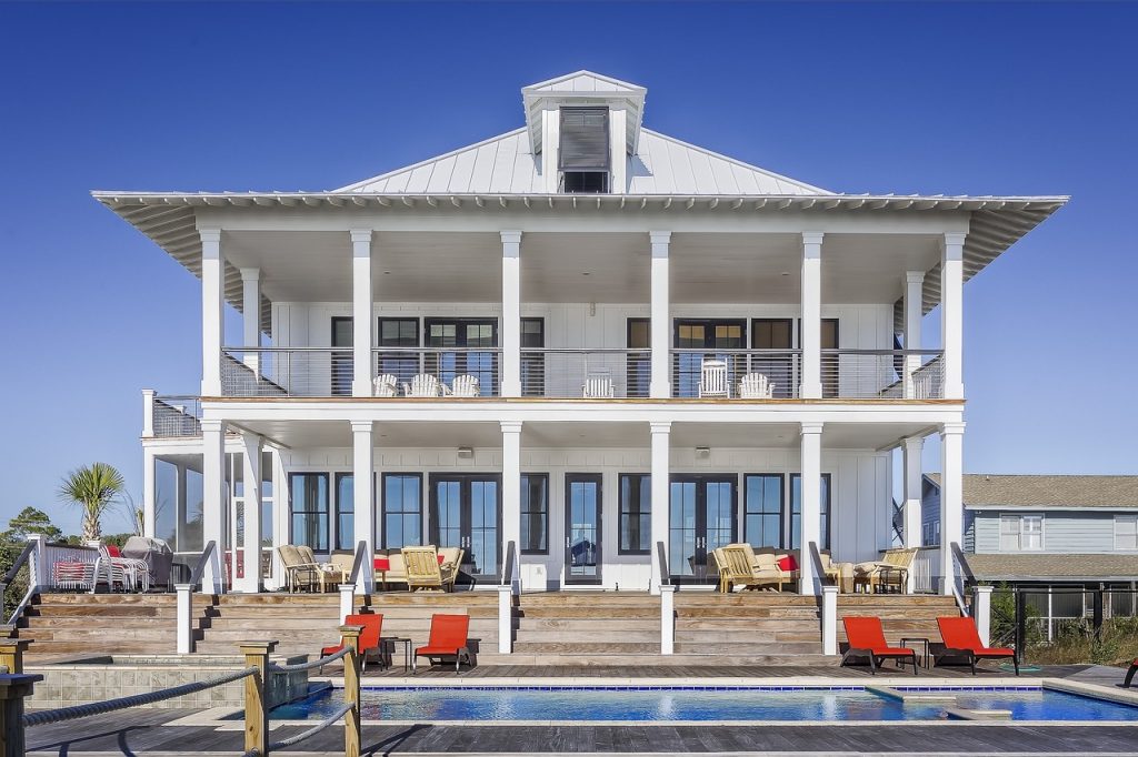 A large white house featuring a swimming pool and a spacious deck, surrounded by a serene outdoor setting